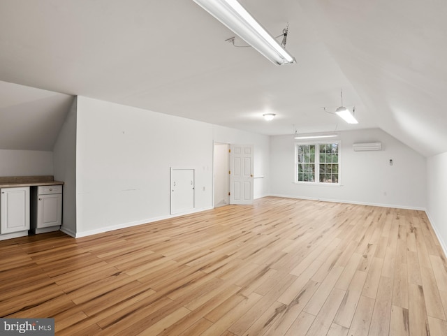 bonus room with lofted ceiling, light wood-type flooring, and a wall unit AC