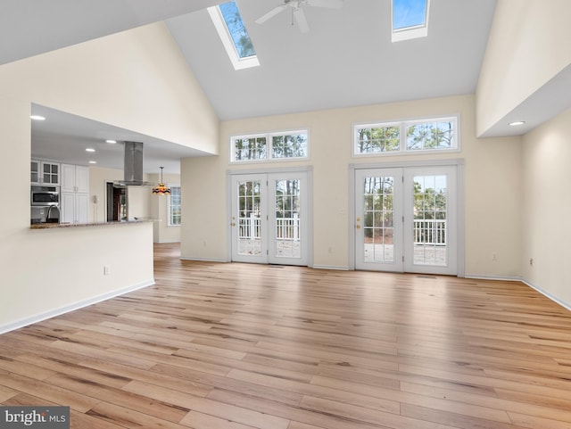 unfurnished living room featuring a towering ceiling, french doors, ceiling fan, and light wood-type flooring