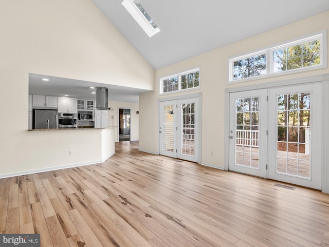 unfurnished living room featuring light hardwood / wood-style floors, a skylight, french doors, and a towering ceiling