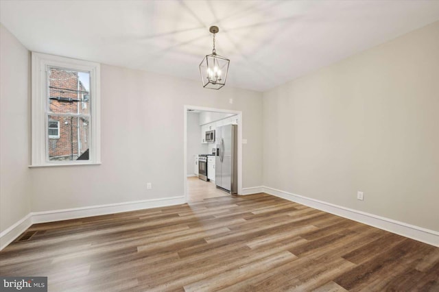 unfurnished dining area with wood-type flooring and a notable chandelier