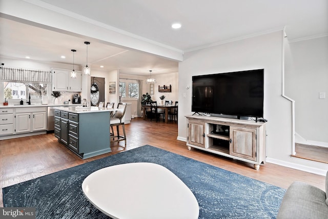 living room featuring sink, wood-type flooring, crown molding, and an inviting chandelier