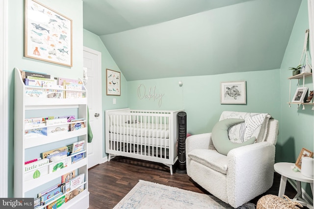 bedroom featuring lofted ceiling, dark wood-type flooring, and a crib