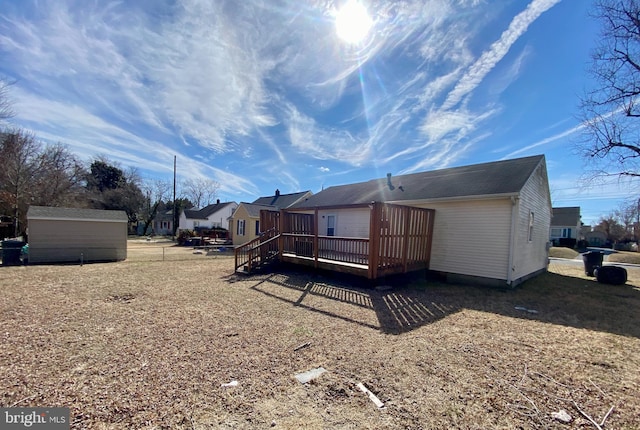 rear view of property featuring an outdoor structure, a wooden deck, and a storage shed