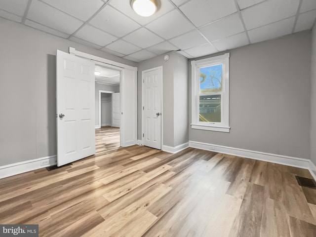 unfurnished bedroom featuring a paneled ceiling, a closet, and wood-type flooring