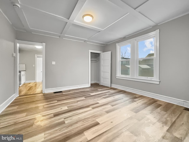 unfurnished bedroom featuring a closet, coffered ceiling, and light wood-type flooring