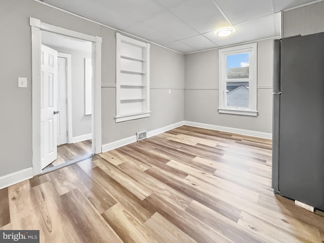 interior space featuring built in shelves, a paneled ceiling, and light hardwood / wood-style flooring