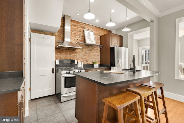 kitchen with a sink, ornamental molding, appliances with stainless steel finishes, wall chimney exhaust hood, and dark countertops