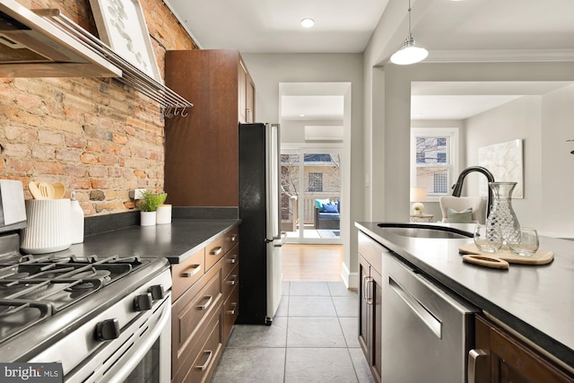 kitchen with light tile patterned floors, dark countertops, appliances with stainless steel finishes, ornamental molding, and a sink