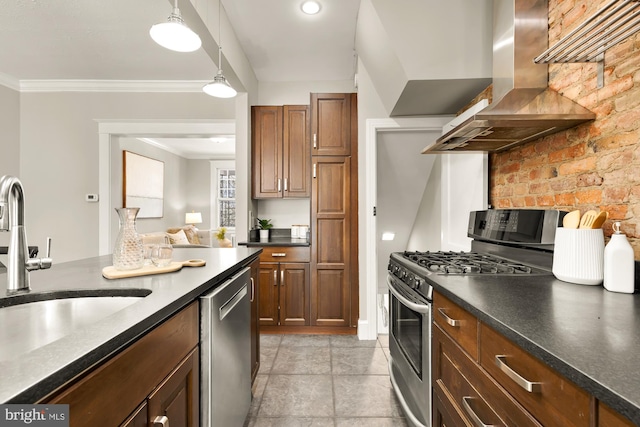 kitchen with dark countertops, wall chimney exhaust hood, ornamental molding, stainless steel appliances, and a sink