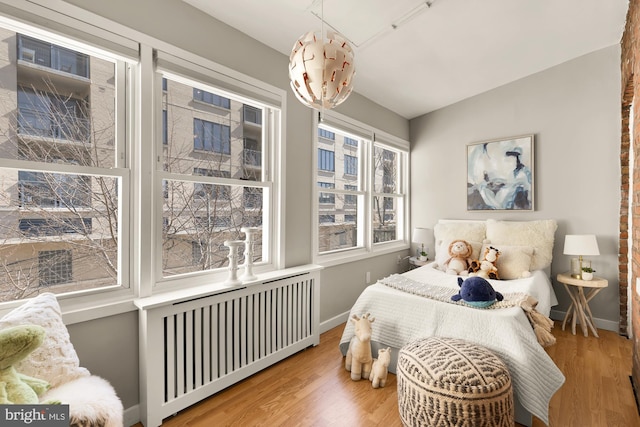 bedroom with radiator, baseboards, vaulted ceiling, and wood finished floors