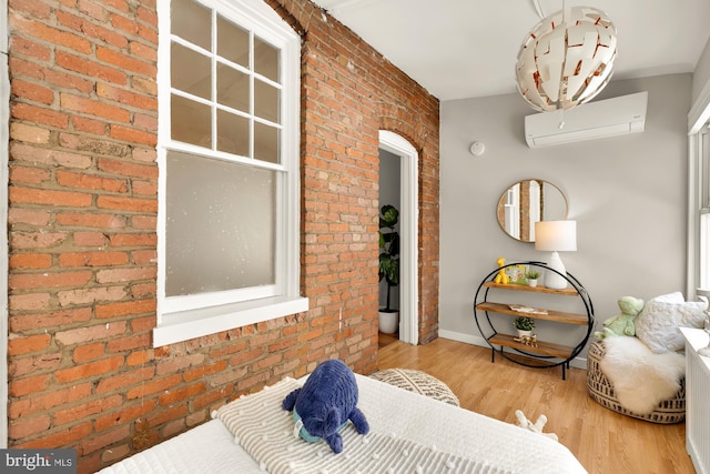 bedroom with brick wall, a wall mounted AC, wood finished floors, and baseboards