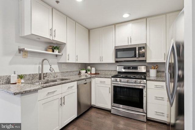 kitchen featuring appliances with stainless steel finishes, light stone counters, dark wood-type flooring, sink, and white cabinets