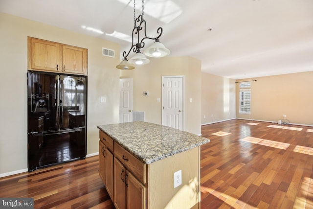 kitchen featuring dark wood-type flooring, light stone counters, a kitchen island, black refrigerator with ice dispenser, and decorative light fixtures