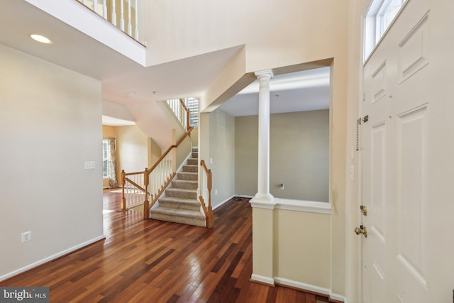 foyer featuring a towering ceiling, decorative columns, dark hardwood / wood-style flooring, and a healthy amount of sunlight