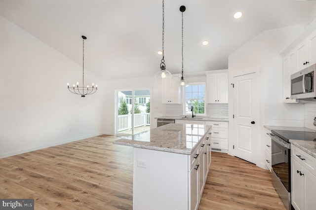 kitchen with white cabinetry, pendant lighting, vaulted ceiling, a kitchen island, and appliances with stainless steel finishes