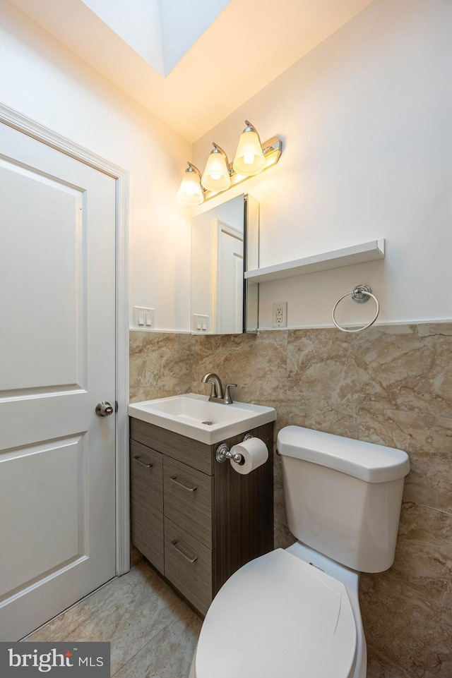 bathroom with vanity, toilet, and tile walls