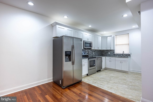 kitchen featuring appliances with stainless steel finishes, tasteful backsplash, dark wood-type flooring, sink, and white cabinetry