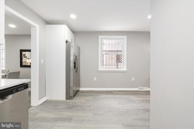 kitchen with stainless steel appliances, white cabinetry, and light hardwood / wood-style flooring