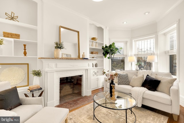 living room with hardwood / wood-style floors, built in shelves, ornamental molding, and a brick fireplace