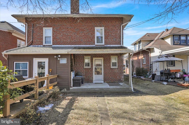 rear view of house with brick siding, a lawn, and a chimney