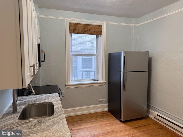 kitchen with a baseboard heating unit, plenty of natural light, light hardwood / wood-style floors, and stainless steel fridge