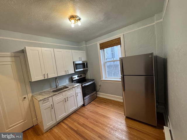 kitchen featuring white cabinetry, appliances with stainless steel finishes, light wood-type flooring, a textured ceiling, and sink