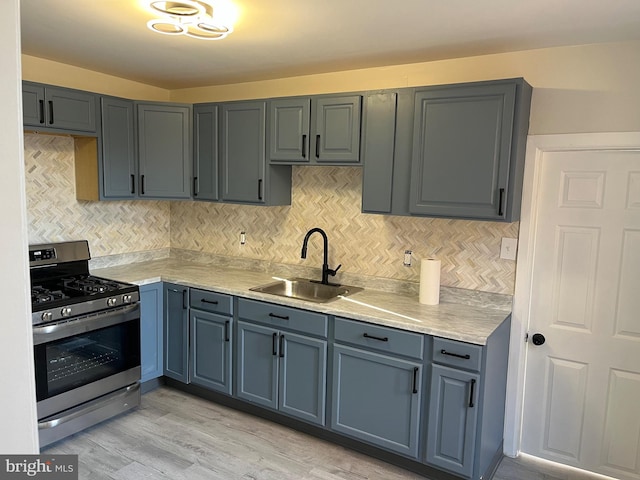 kitchen with tasteful backsplash, sink, light wood-type flooring, and stainless steel gas range