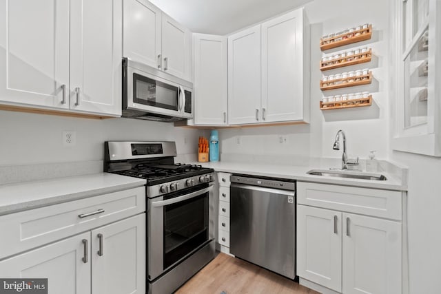 kitchen with white cabinets, appliances with stainless steel finishes, light hardwood / wood-style flooring, and sink