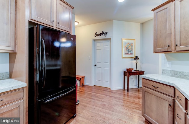 kitchen with black fridge, light hardwood / wood-style floors, and light stone countertops