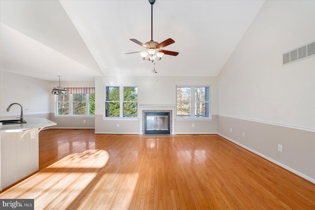 unfurnished living room with ceiling fan, vaulted ceiling, light hardwood / wood-style flooring, and sink