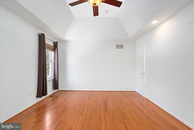 empty room with light hardwood / wood-style floors, ceiling fan, and a tray ceiling