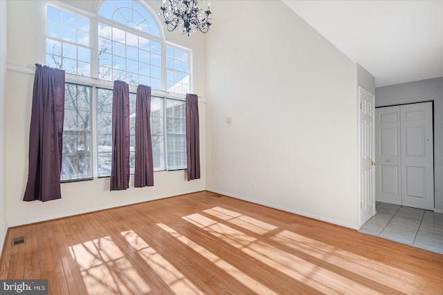 empty room with an inviting chandelier, a towering ceiling, plenty of natural light, and wood-type flooring