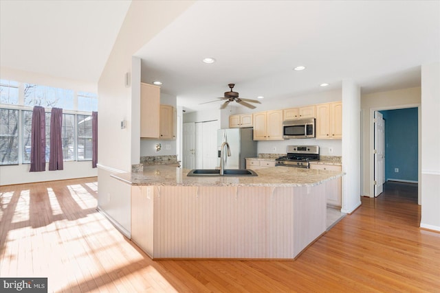 kitchen featuring appliances with stainless steel finishes, light wood-type flooring, light stone countertops, kitchen peninsula, and sink