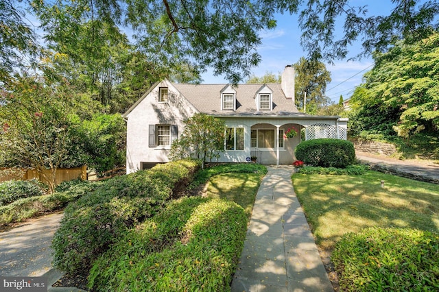 cape cod house with covered porch, fence, stucco siding, a front lawn, and a chimney