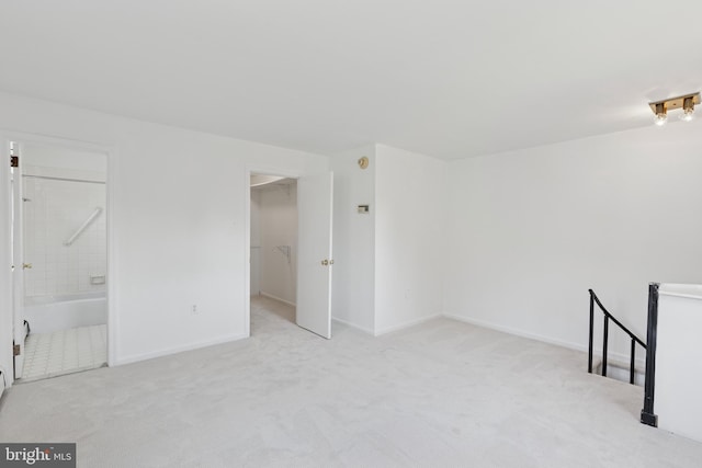 unfurnished bedroom featuring baseboards, a walk in closet, connected bathroom, and light colored carpet