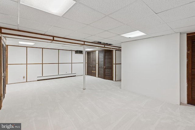 finished basement featuring light carpet, visible vents, a baseboard heating unit, and a drop ceiling