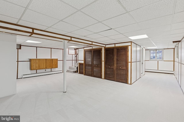 basement with a baseboard heating unit, a paneled ceiling, and light colored carpet