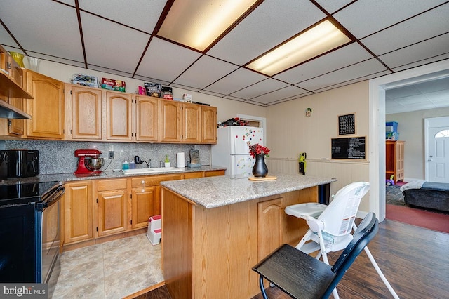 kitchen featuring sink, black range with electric cooktop, white fridge, a kitchen bar, and a kitchen island