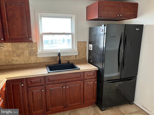 kitchen with black fridge, light tile patterned floors, decorative backsplash, and sink