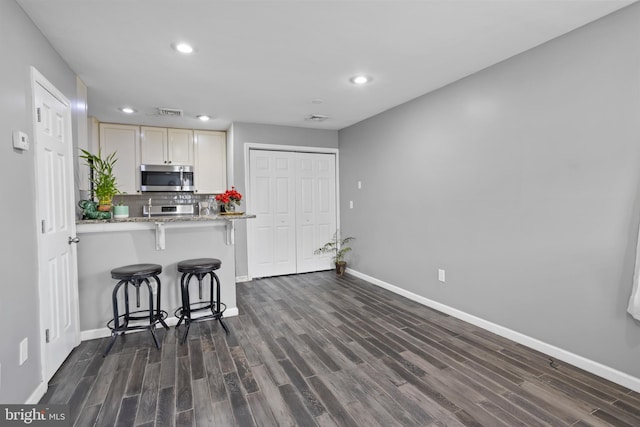 kitchen featuring a kitchen bar, kitchen peninsula, backsplash, dark hardwood / wood-style flooring, and light stone countertops