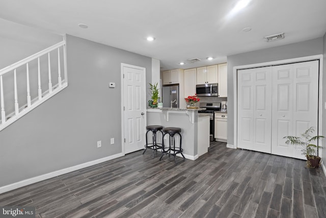 kitchen with appliances with stainless steel finishes, dark wood-type flooring, tasteful backsplash, light stone counters, and a breakfast bar area