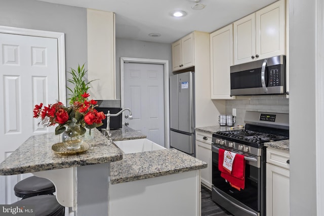 kitchen featuring a kitchen bar, stainless steel appliances, tasteful backsplash, light stone countertops, and sink