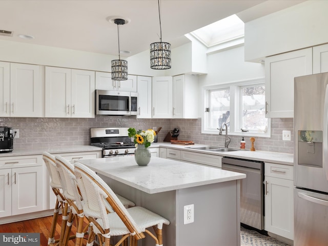 kitchen with tasteful backsplash, appliances with stainless steel finishes, a center island, white cabinets, and sink