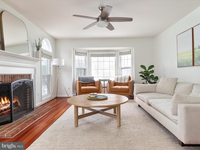 living room with ceiling fan, a brick fireplace, and dark hardwood / wood-style floors