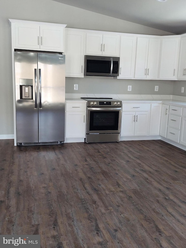 kitchen featuring dark hardwood / wood-style floors, white cabinets, stainless steel appliances, and vaulted ceiling