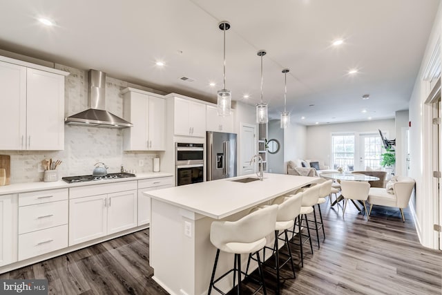 kitchen featuring wall chimney exhaust hood, sink, white cabinetry, stainless steel appliances, and a kitchen island with sink