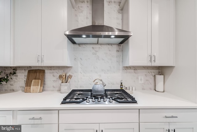 kitchen featuring tasteful backsplash, wall chimney exhaust hood, stainless steel gas stovetop, and white cabinets