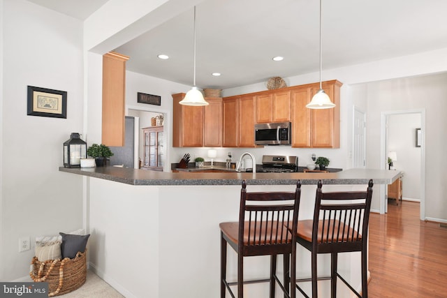 kitchen with a breakfast bar, hanging light fixtures, light wood-type flooring, appliances with stainless steel finishes, and kitchen peninsula