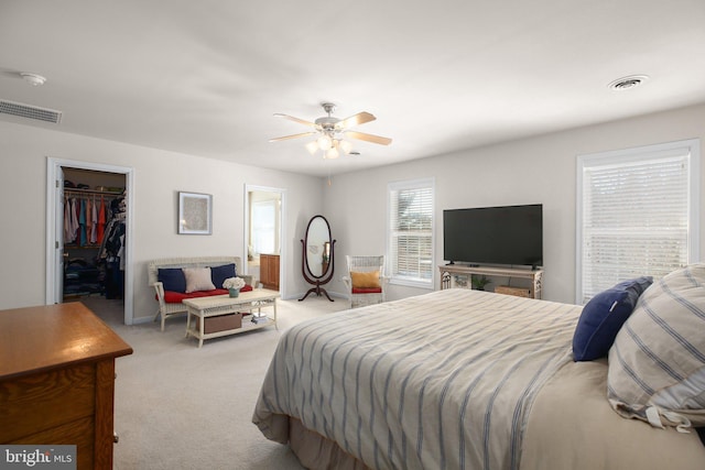 bedroom featuring a walk in closet, light colored carpet, a closet, and ceiling fan