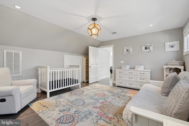 bedroom featuring dark hardwood / wood-style flooring, a nursery area, and vaulted ceiling